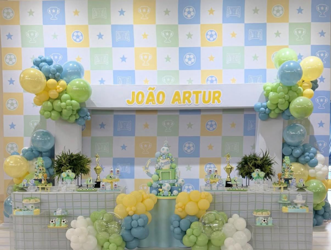 Cenário completo de festa em tons suaves com flores, mesa de doces e painéis decorados