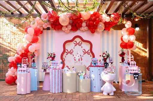 Ambientação completa de festa com arco de balões rosados, painel e mesas decoradas